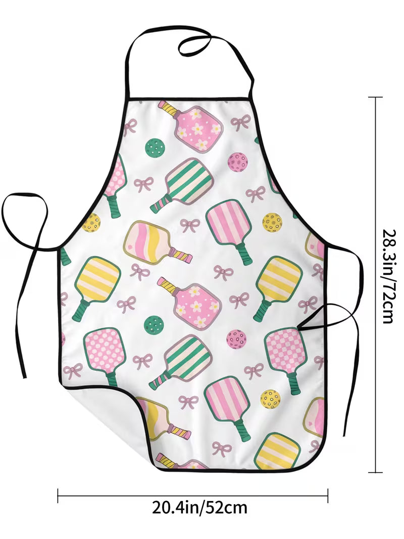 A white apron with a colorful pattern of retro paddle-shaped candies, bows, and dots, shown with black neck and waist ties. Measurement lines indicate dimensions of 28.