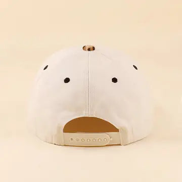 A white baseball cap shown from the back, featuring black ventilation eyelets and a tan adjustable snap closure, set against a solid cream background.