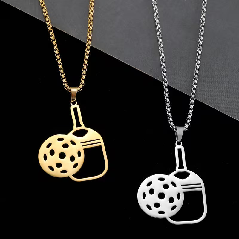 Two stainless steel pendant necklaces displayed side by side on a black background. One necklace is gold-toned and the other is silver-toned, both featuring a pendant shaped like a perforated golf ball overlapping a bottle opener.