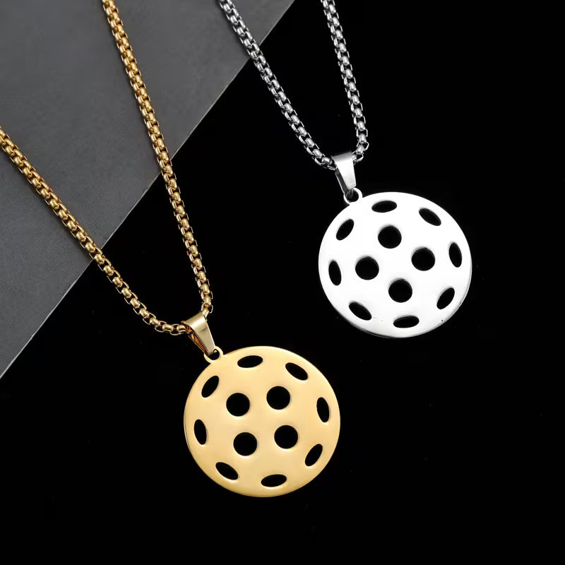 Two round pendant necklaces with perforated circular designs, one in gold and one in silver, displayed on black and dark gray backgrounds.