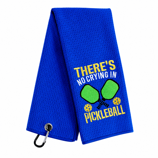 A royal blue mesh golf towel with a black carabiner clip, featuring a yellow and white embroidered design that reads 'THERE'S NO CRYING IN PICKLEBALL' with two green pickleballs, on a white background.