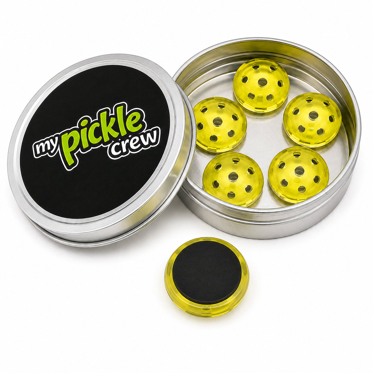 A round silver metal tin with its lid off, showing five translucent yellow pickle balls inside and a separate matching lid in front. The lid features a black label with the text 'my pickle crew' in green and white.