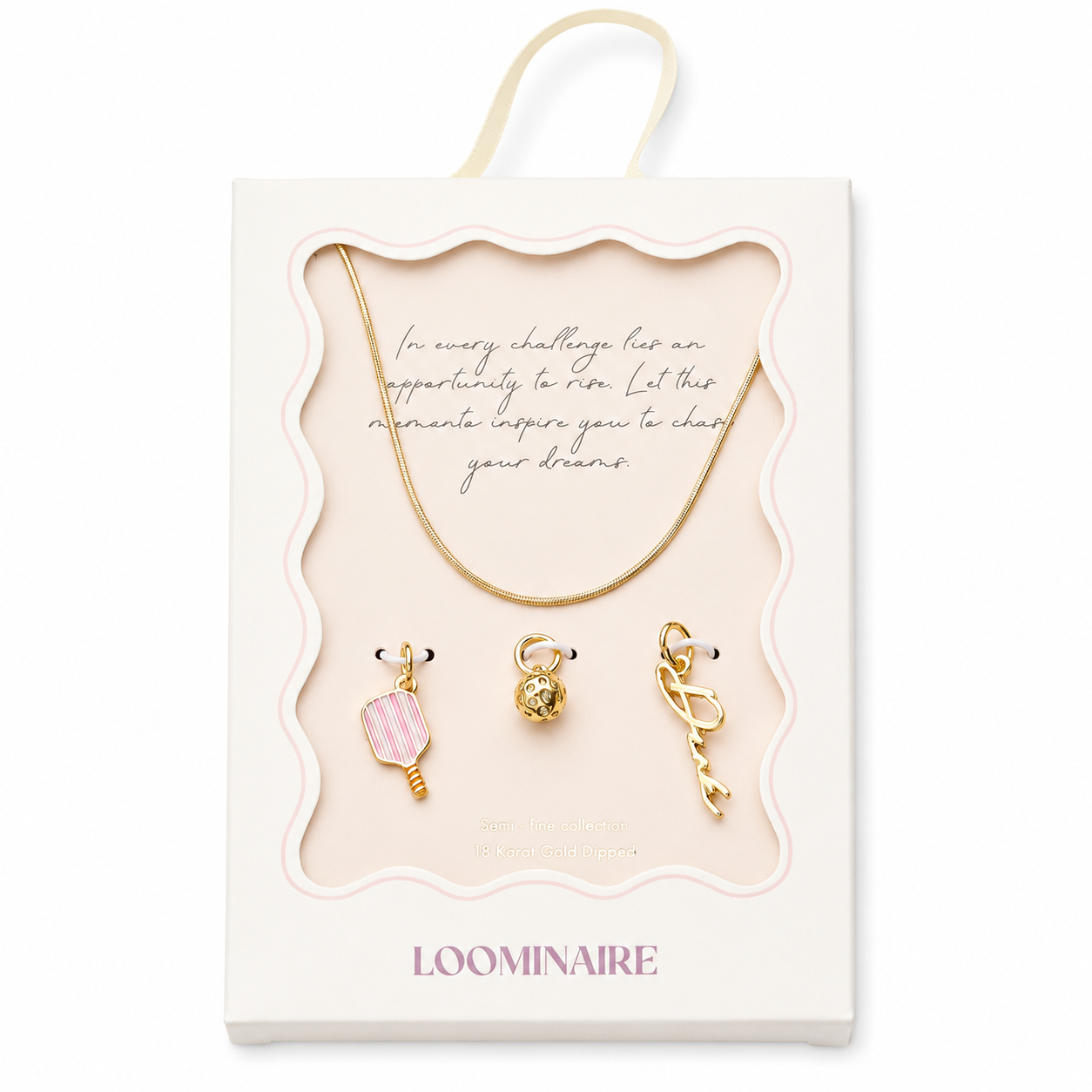 A boxed jewelry set from Loominaire featuring a gold necklace and three gold charms with pink and gold details, presented in a cream-colored display box with a hanging loop.