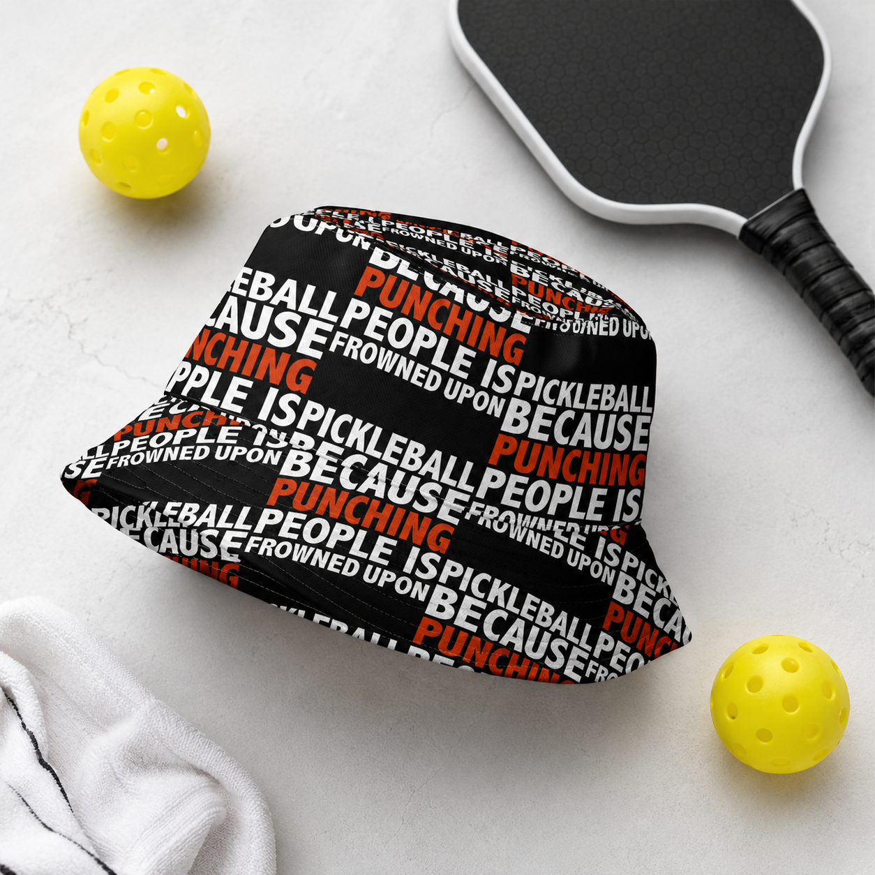 Funny pickleball bucket hat flat lay with pickleball paddle, balls and towel