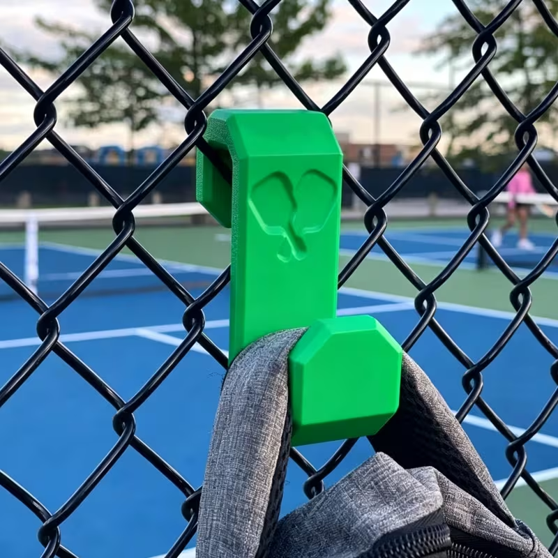 Green pickleball fence hook holding a bag on a pickleball court fence