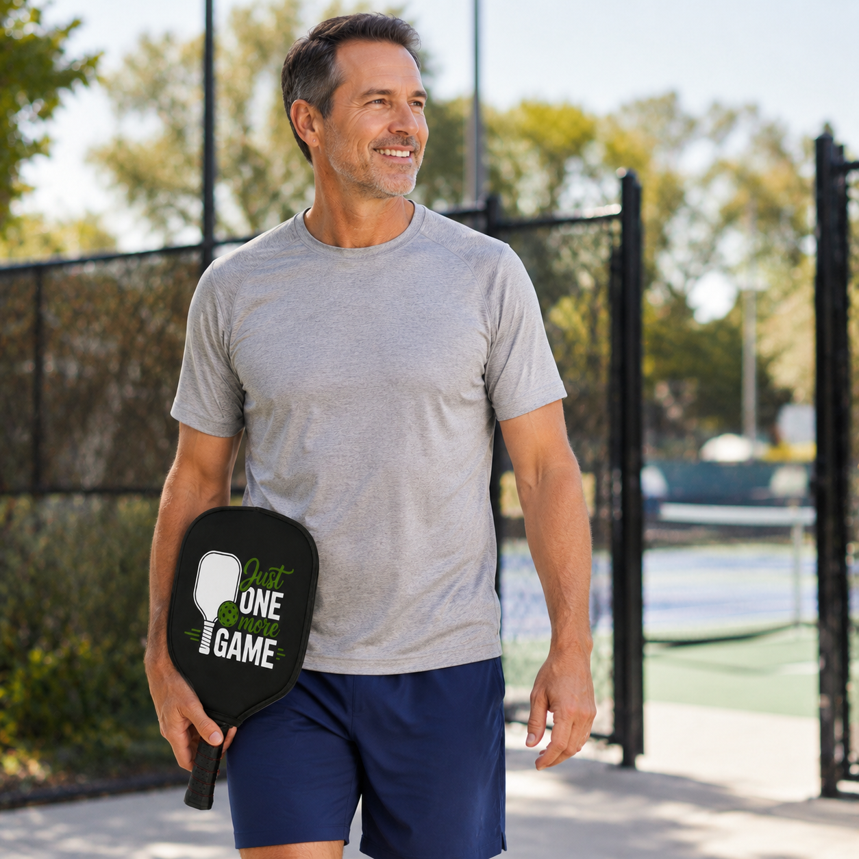 Man carrying a Just One More Game pickleball paddle cover to the court