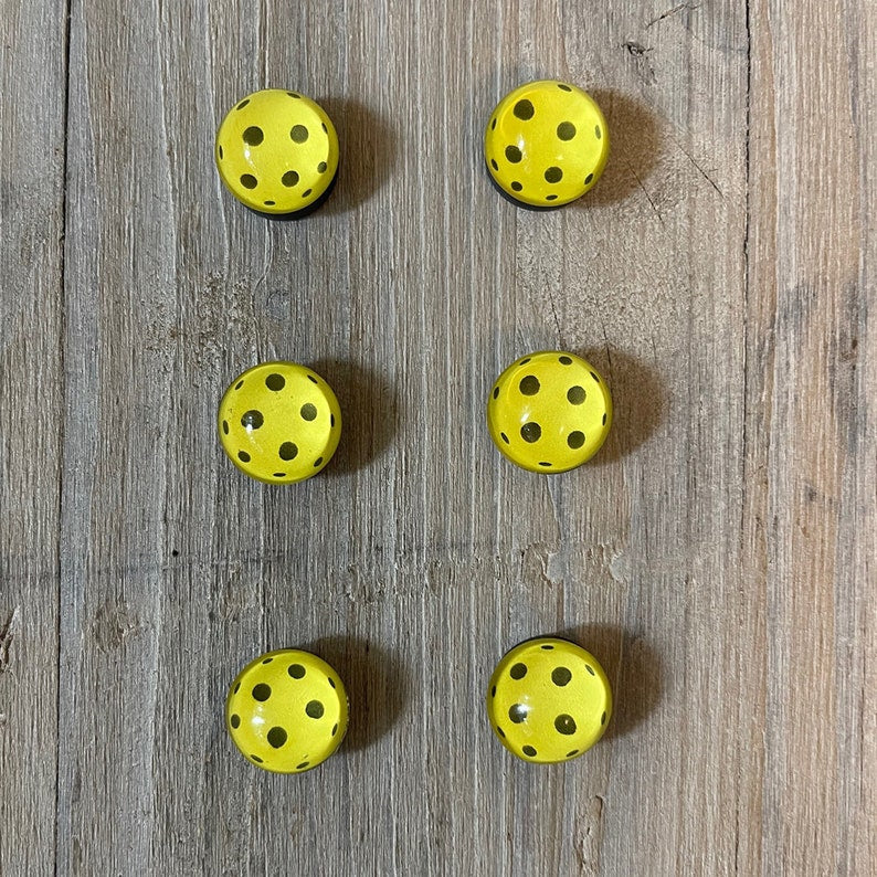 Six yellow pickleball magnets on wood background
