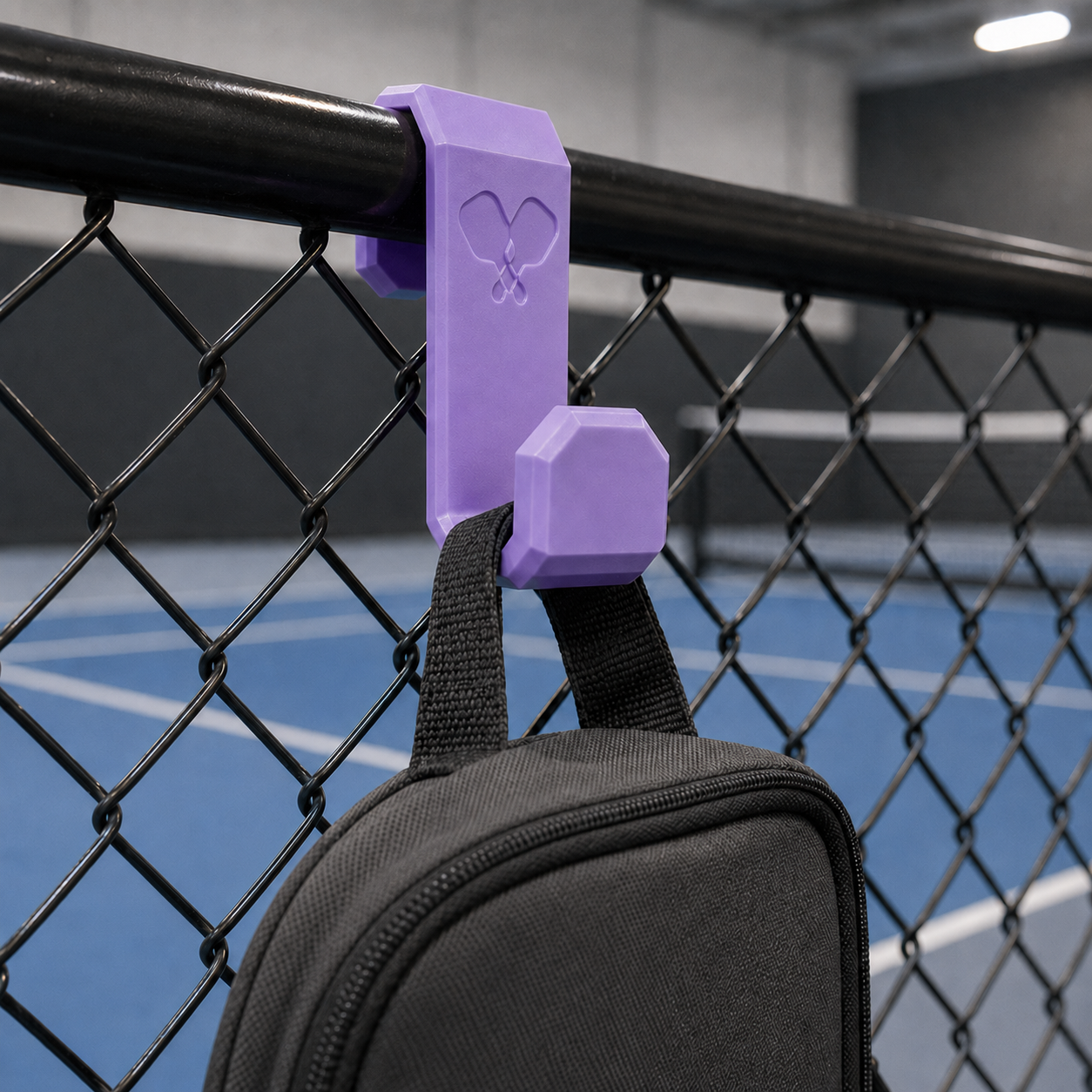 Purple pickleball fence hook holding a paddle bag at an indoor pickleball court